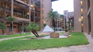 Edifici d'altes plantes amb balcons, una font central i un pati ben cuidat amb vegetació.