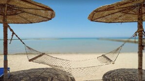 Een strandgezicht met twee rieten parasols en een hangmat ertussen.