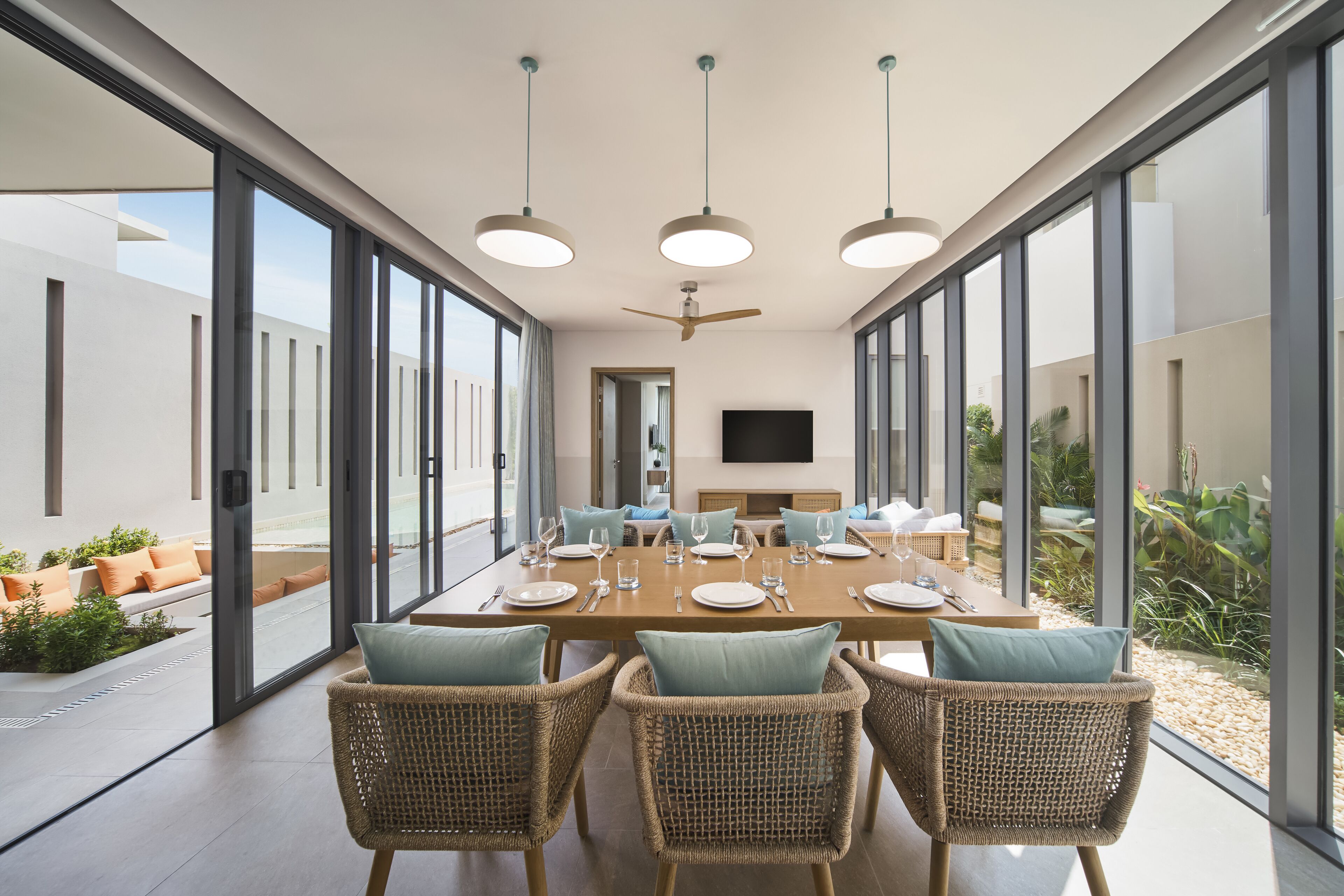 A modern dining area with a long table, wicker chairs, and a flat-screen TV mounted on the wall.