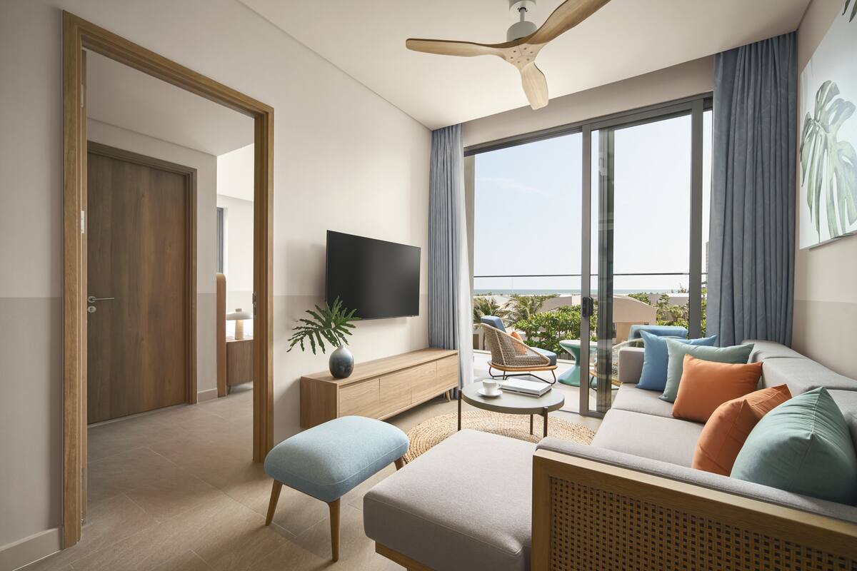 A modern living room with a flat-screen TV, a sofa with cushions, a coffee table, and a ceiling fan.