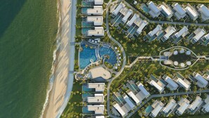 An aerial view of a resort with multiple buildings, a central swimming pool, and a beach. - IXORA Ho Tram By Fusion (Ho Chi Minh City)