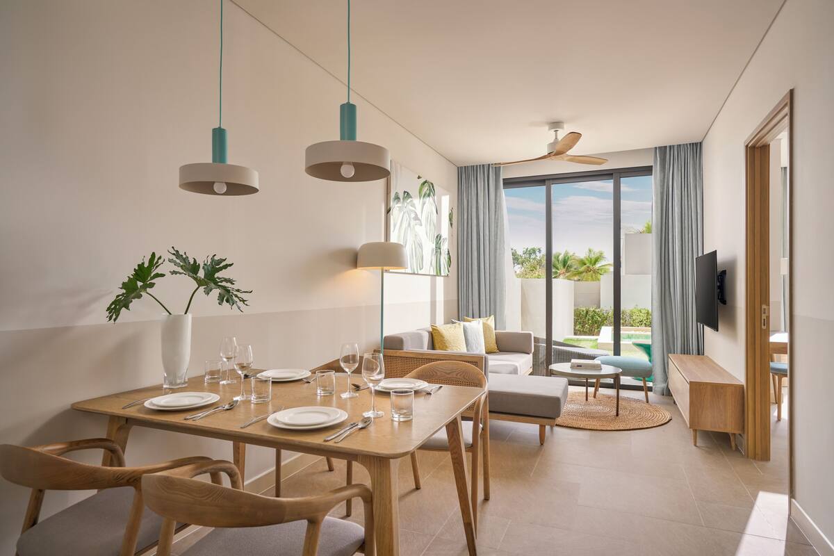A modern dining area with a wooden table set for four, a sofa, and a TV mounted on the wall.