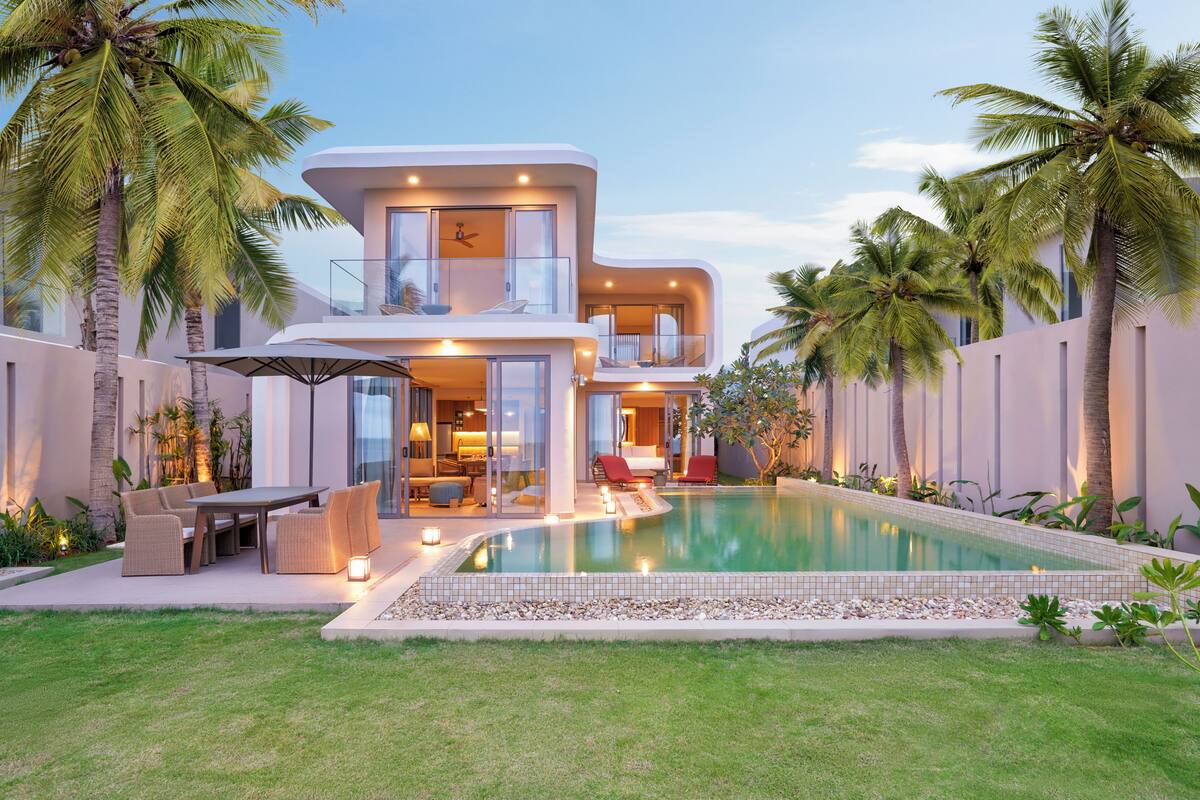 A modern two-story house with a swimming pool, outdoor seating, and palm trees.