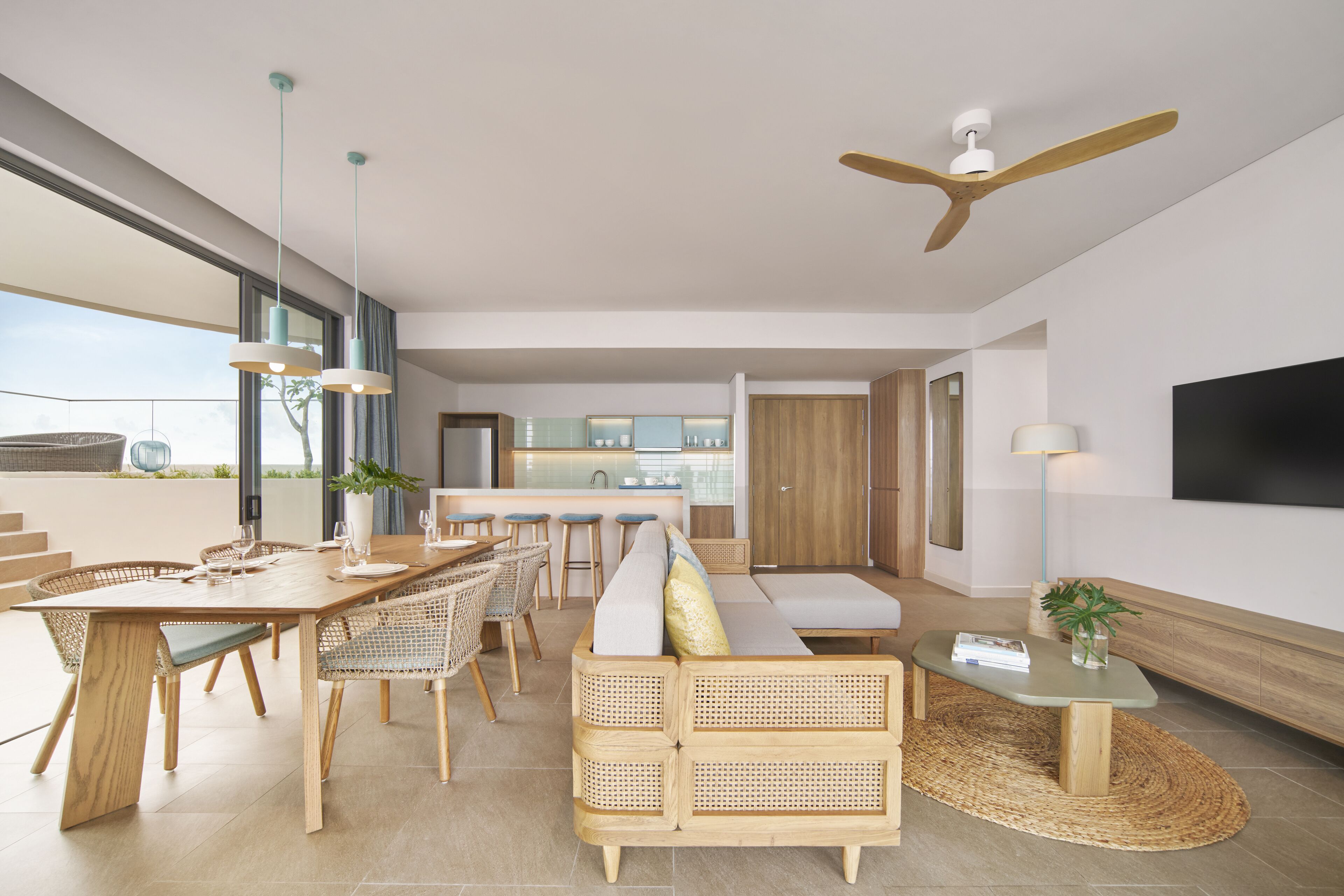 A modern living room with a wooden dining table, wicker chairs, a sofa, and a ceiling fan.