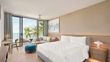A modern hotel room with a large bed, a seating area with a view of the ocean, a dining table, and a small balcony.