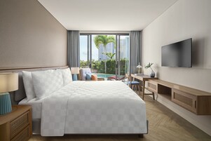 Une chambre d’hôtel avec un grand lit, un bureau, une télévision et une vue sur les palmiers et les immeubles.