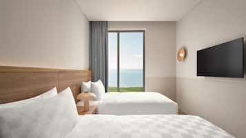 A hotel room with two beds, a large window with a view of the sea, a flat-screen TV, and a wooden headboard.