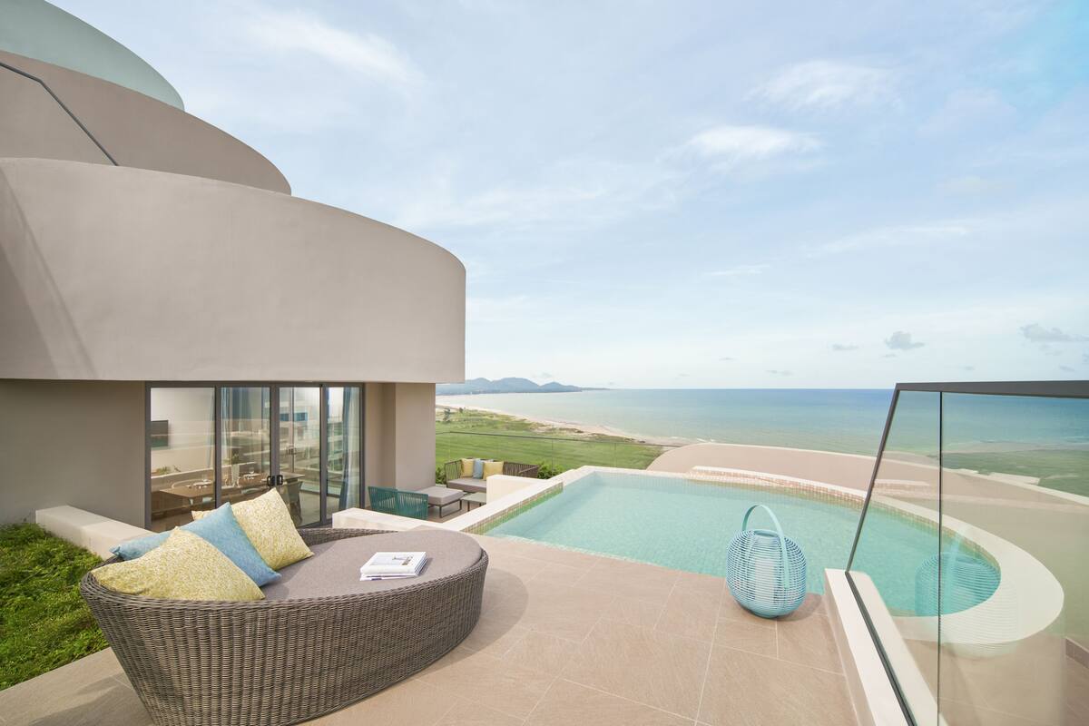 A modern outdoor lounge area with a pool, comfortable seating, and a scenic ocean view.