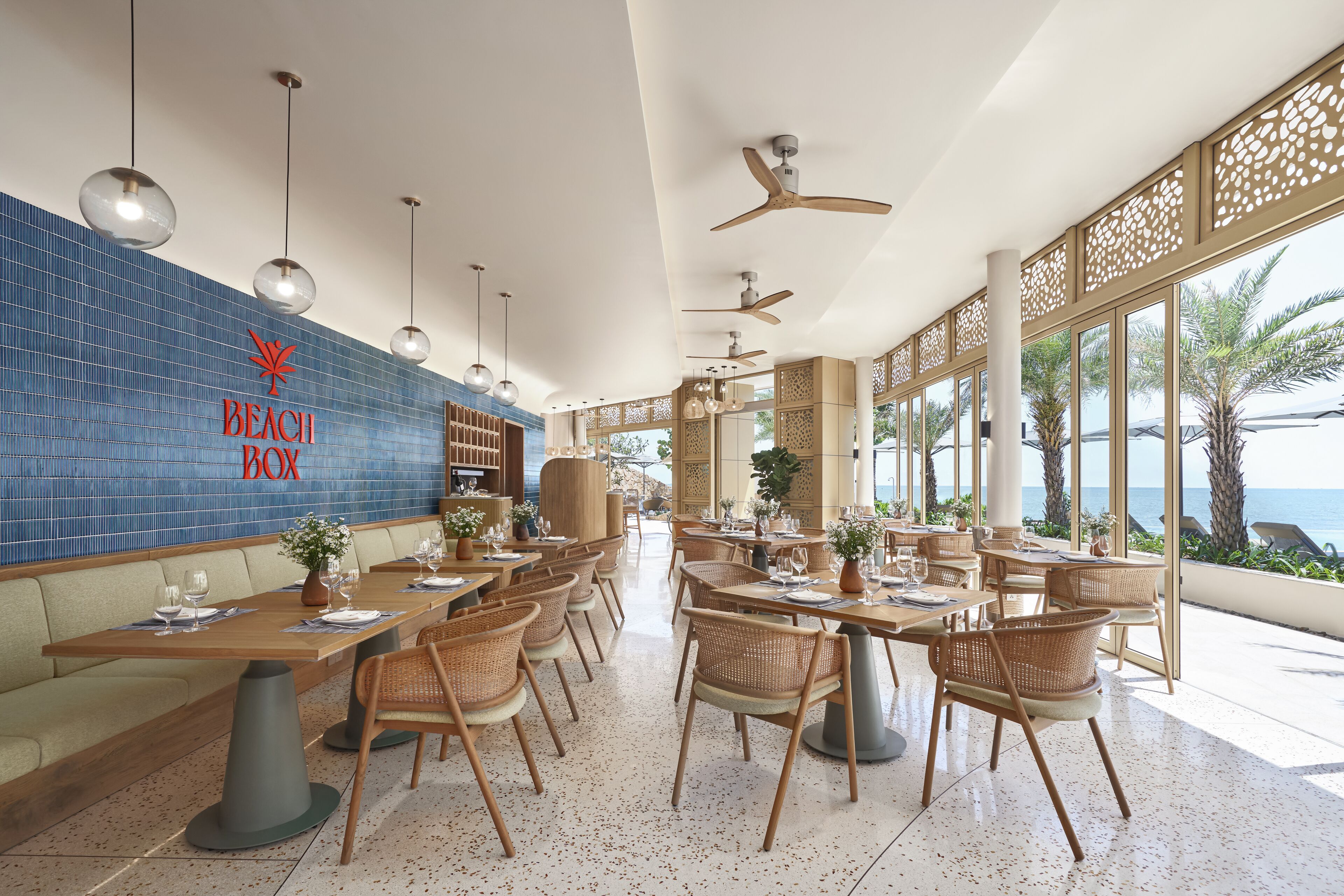 A spacious dining area with high ceilings, ceiling fans, and large windows offering a view of the sea.