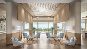 A spacious lobby with wicker chairs, round tables, and large windows offering a view of the outdoors. - IXORA Ho Tram By Fusion (Ho Chi Minh City)