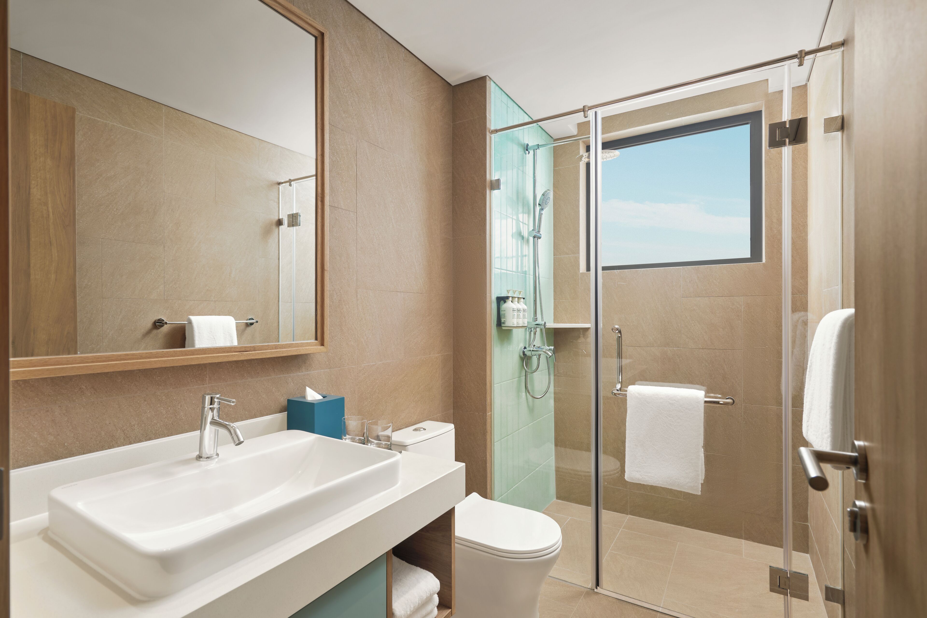 Un baño moderno con un espejo grande, un lavabo blanco, un inodoro y una ducha con mampara de vidrio.