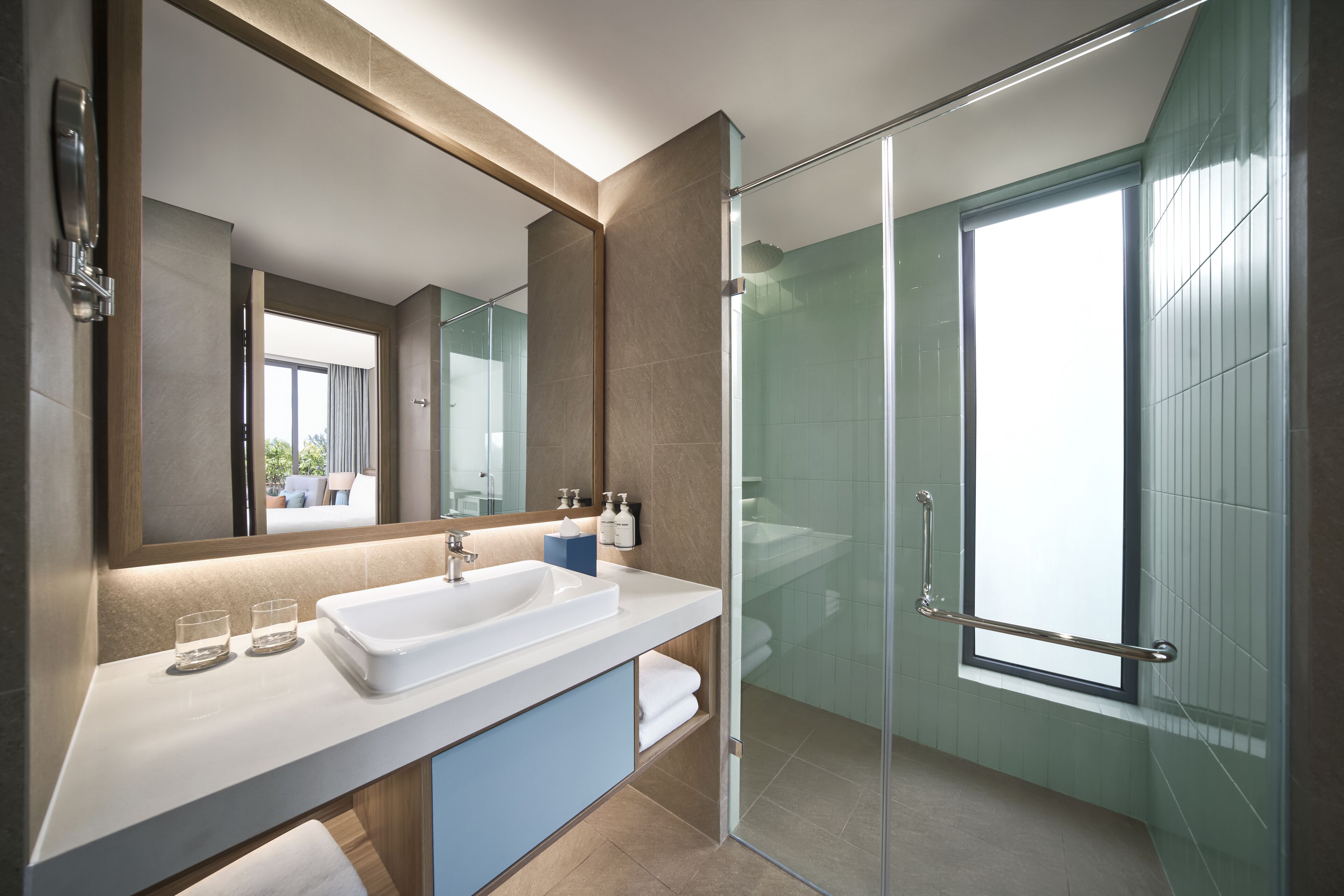 Un baño moderno con ducha envuelta en vidrio, un espejo grande y un lavamanos blanco.