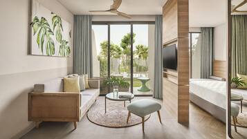 A modern hotel room with a sofa, a round coffee table, a TV, and a bed.