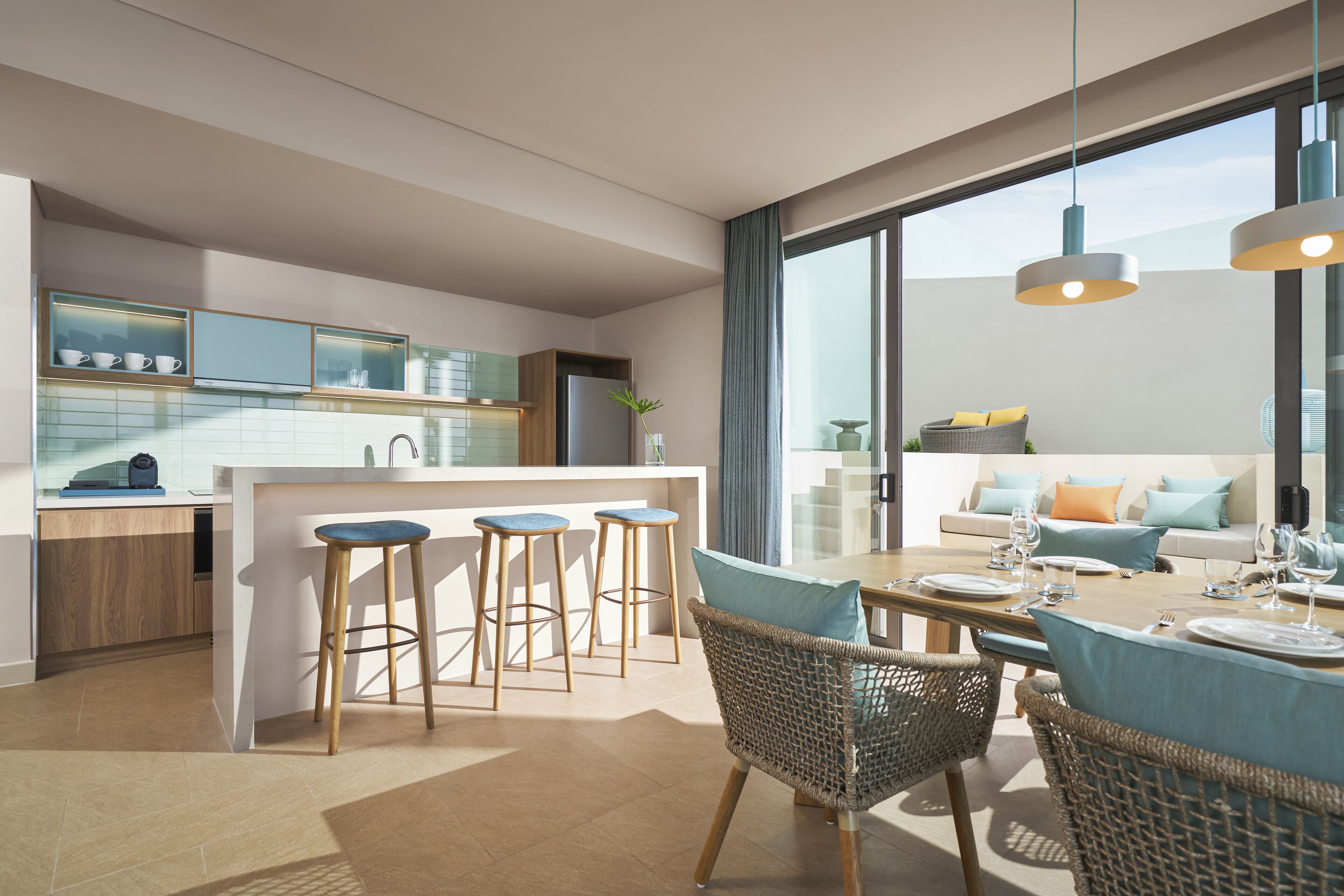 A modern kitchen with bar stools, a dining area with wicker chairs, and a large window offering a view of the city.