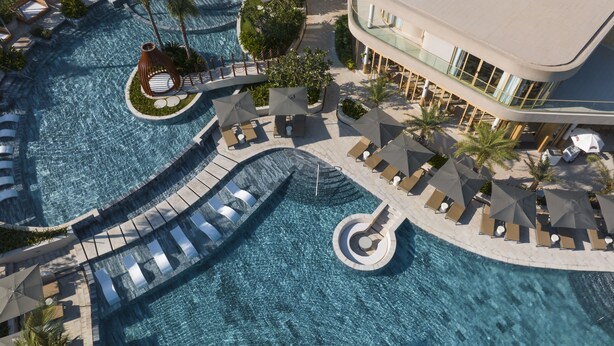 An aerial view of a resort with a large swimming pool, sun loungers, and palm trees. - IXORA Ho Tram By Fusion (Ho Chi Minh City)