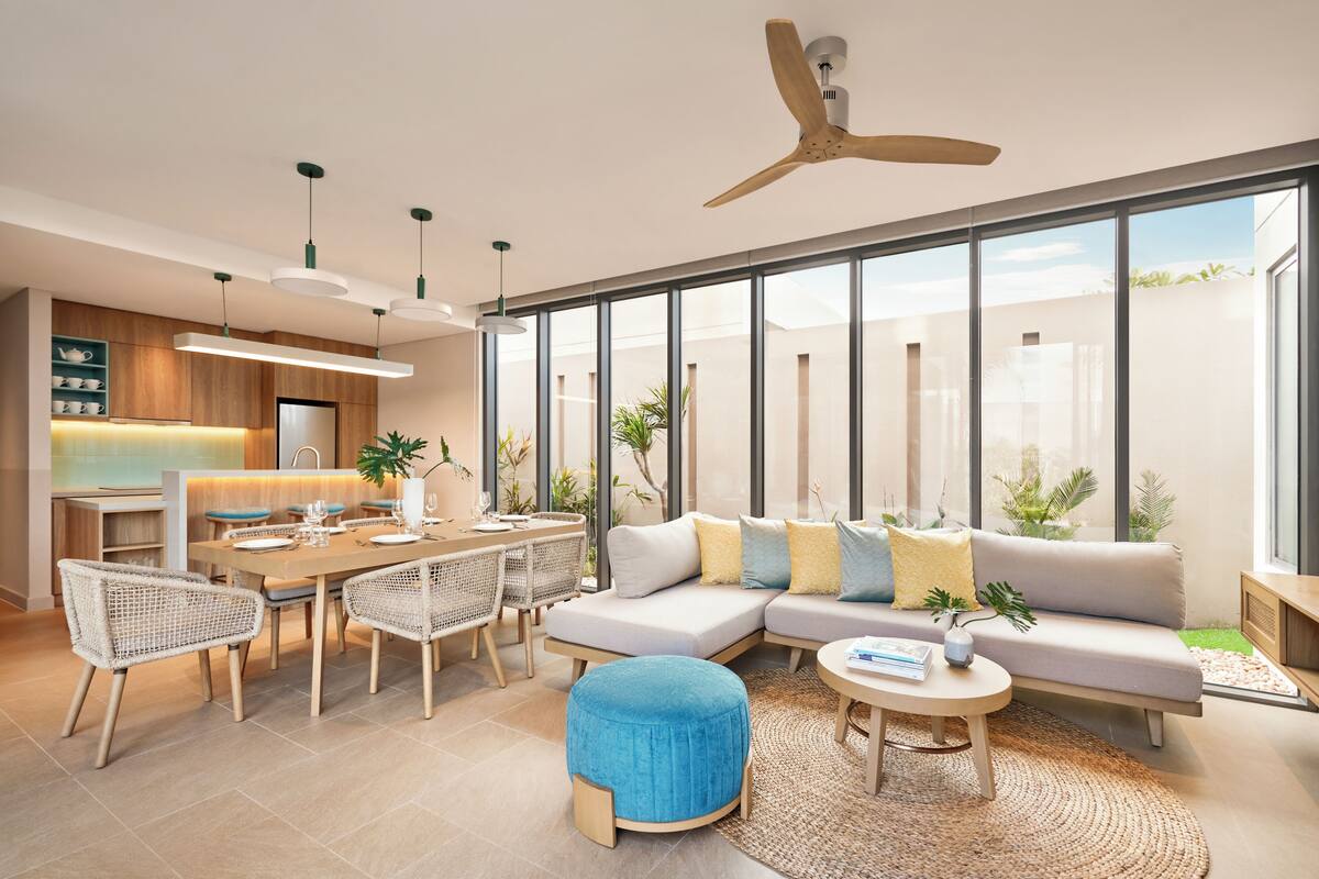 A modern living room with a dining area, large windows, and a ceiling fan.