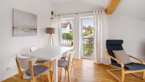 Een eethoek met een witte tafel en stoelen, een blauw bekleden fauteuil, een lamp en uitzicht door een glazen deur.
