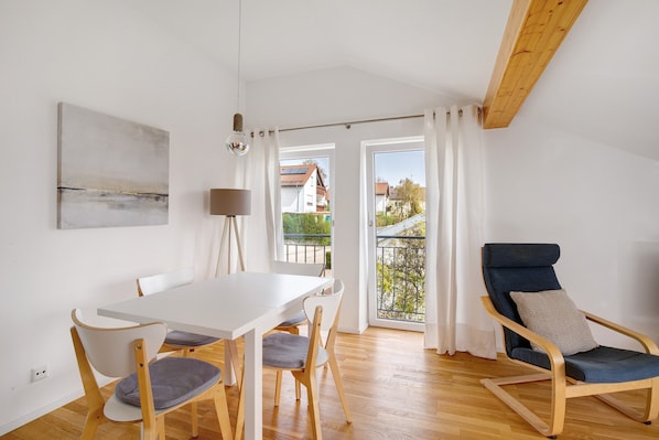 A dining area with a white table and chairs, a blue cushioned chair, a lamp, and a view through a glass door.