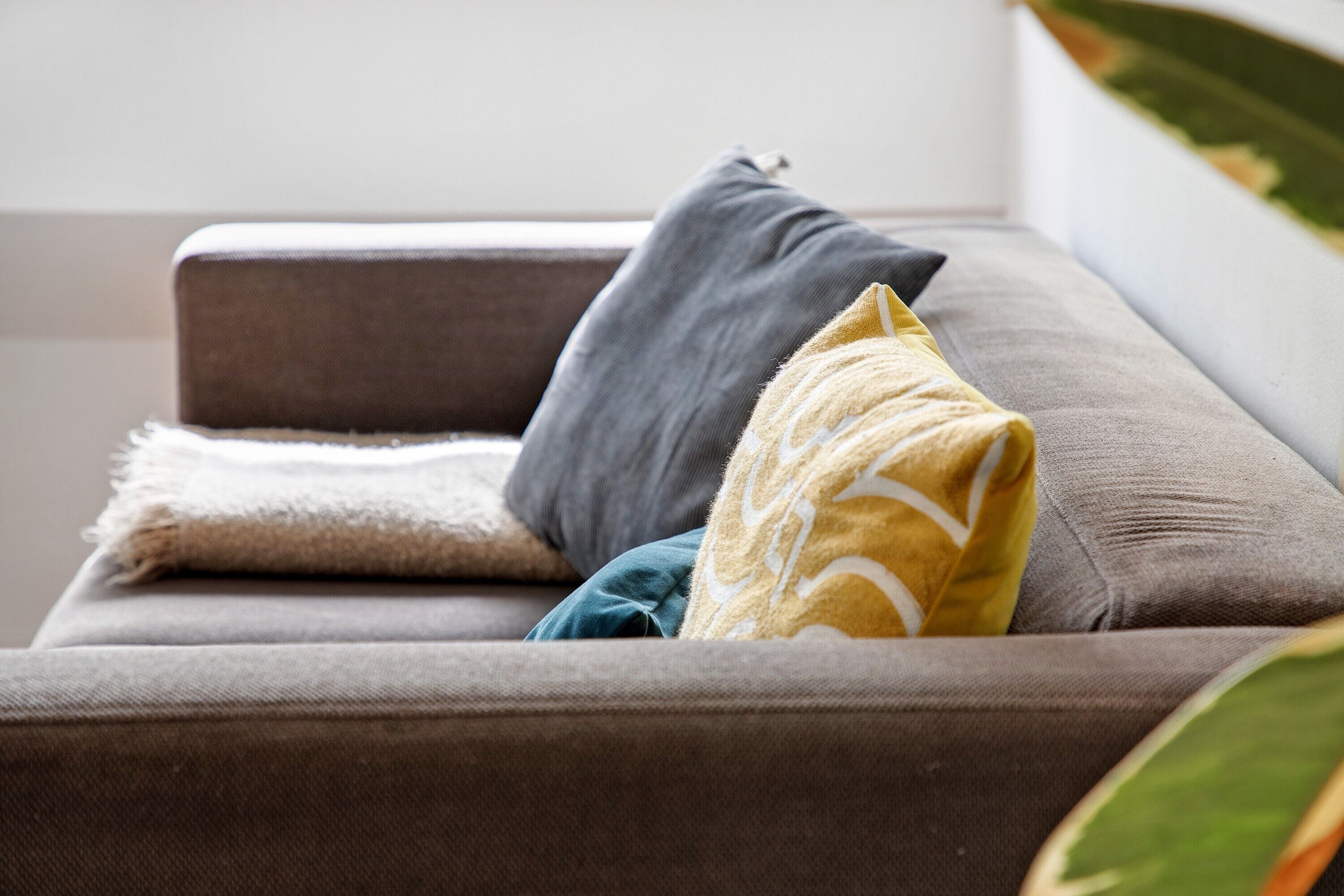 Ein braunes Sofa mit einer weißen Decke und zwei Kissen, eines grau und eines gelb.