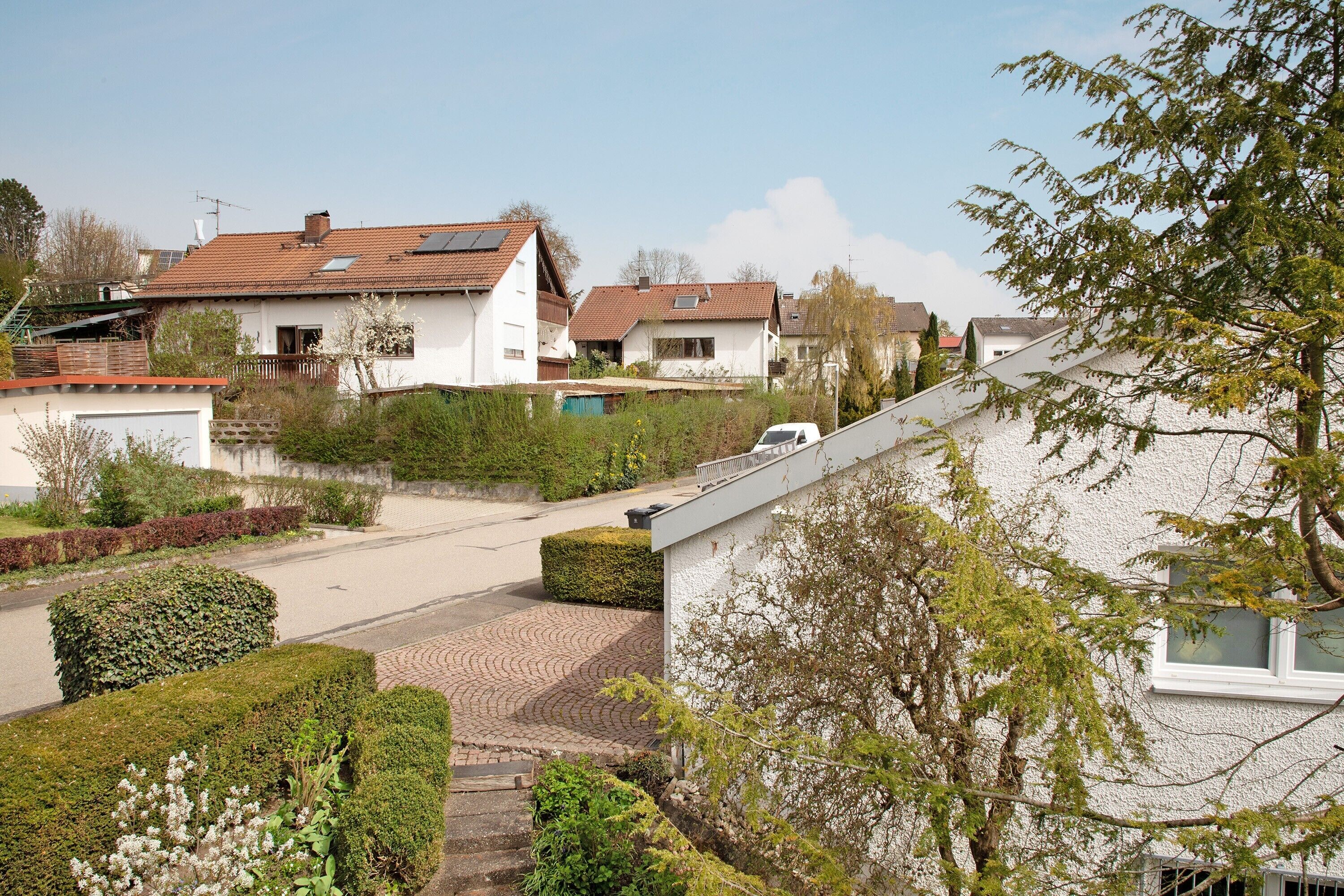 Eine Wohnstraße mit Häusern, einem gepflasterten Auffahrt und einem am Straßenrand geparkten Auto.