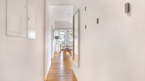 Een gang met houten vloer, witte muren en een eetgedeelte met een tafel en stoelen.