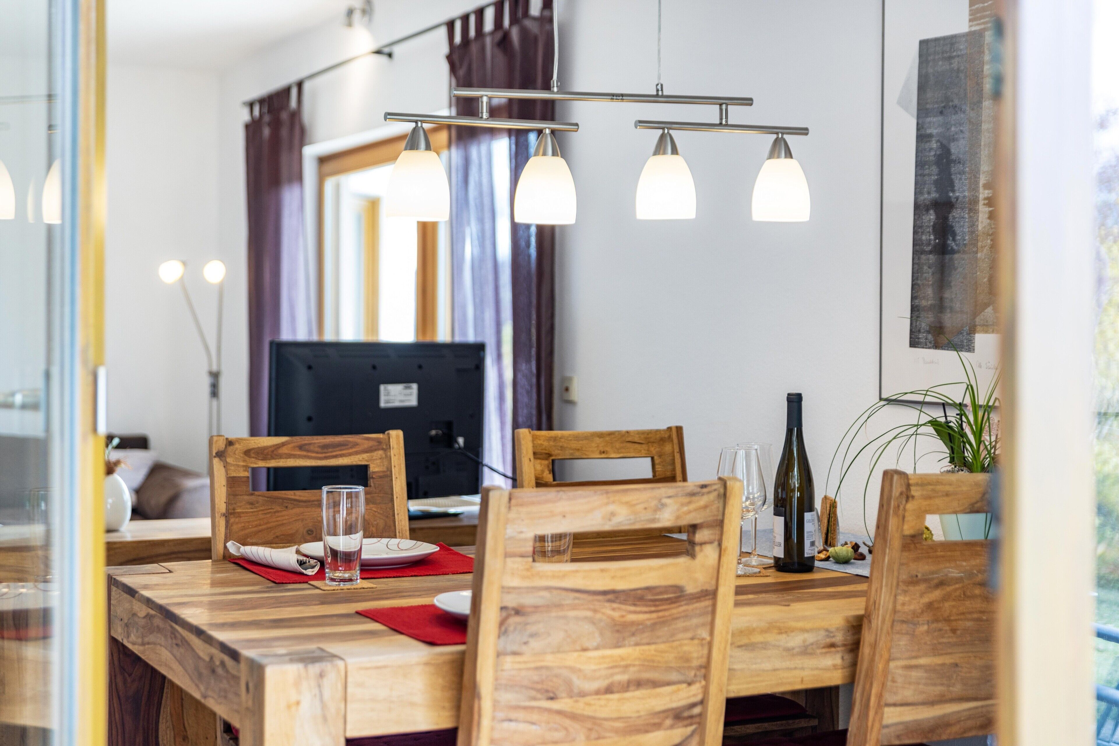 A dining area with a wooden table, chairs, a computer, and a wine bottle.