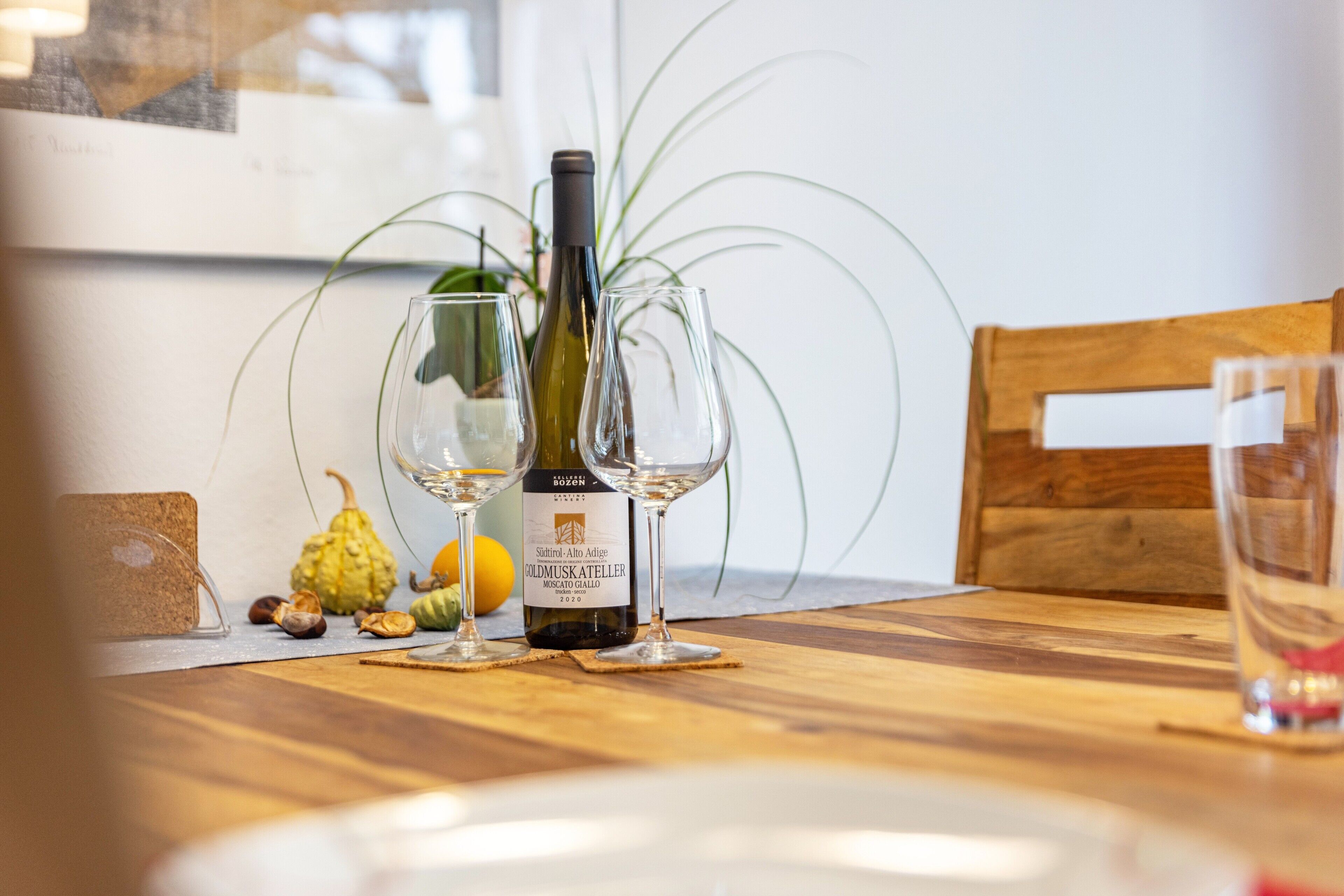 Una mesa de madera con una botella de vino, dos copas de vino y una planta en maceta.