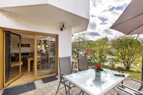 A patio with a glass table, chairs, and a potted plant.