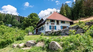 A traditional chalet with a sloped roof, stone foundation, and a cross on the front wall.
