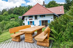 Una casa con techo rojo, una banca de madera y una mesa de picnic al frente.
