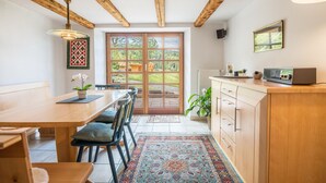 A kitchen with wooden beams, a dining area with chairs, a large window, and a radiator.