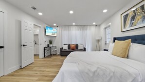 A modern hotel room with a large bed, a TV mounted on the wall, a desk with a chair, and a view of the beach through the curtains. - Wilderness Escape, by Breathtaking Natl Park (Tampa)