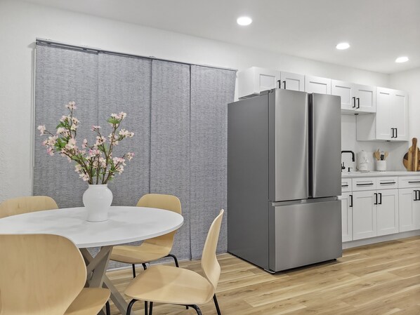Una cocina moderna con armarios blancos, un refrigerador de acero inoxidable y una zona de comedor con mesa y sillas blancas.