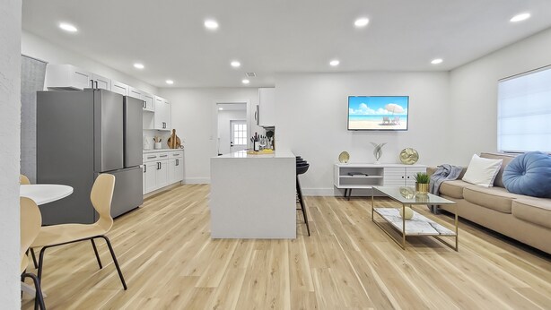 A modern kitchen with white cabinets, a large refrigerator, and a wooden dining table with chairs. - Wilderness Escape, by Breathtaking Natl Park (Tampa)