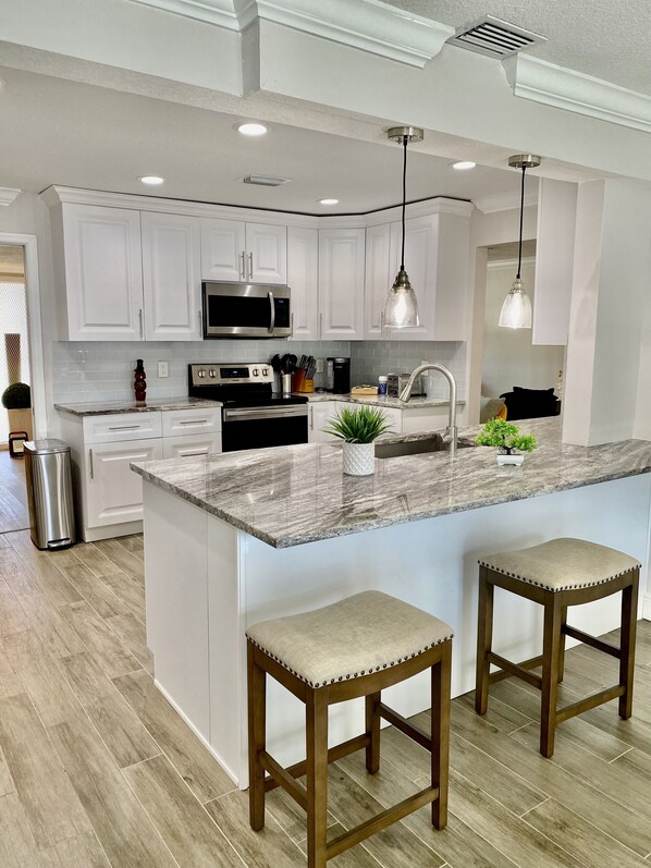 A modern kitchen with white cabinets, stainless steel appliances, a marble countertop, and pendant lighting.
