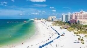 A beach with a long stretch of white sand, a clear blue ocean, and a row of hotels in the background.