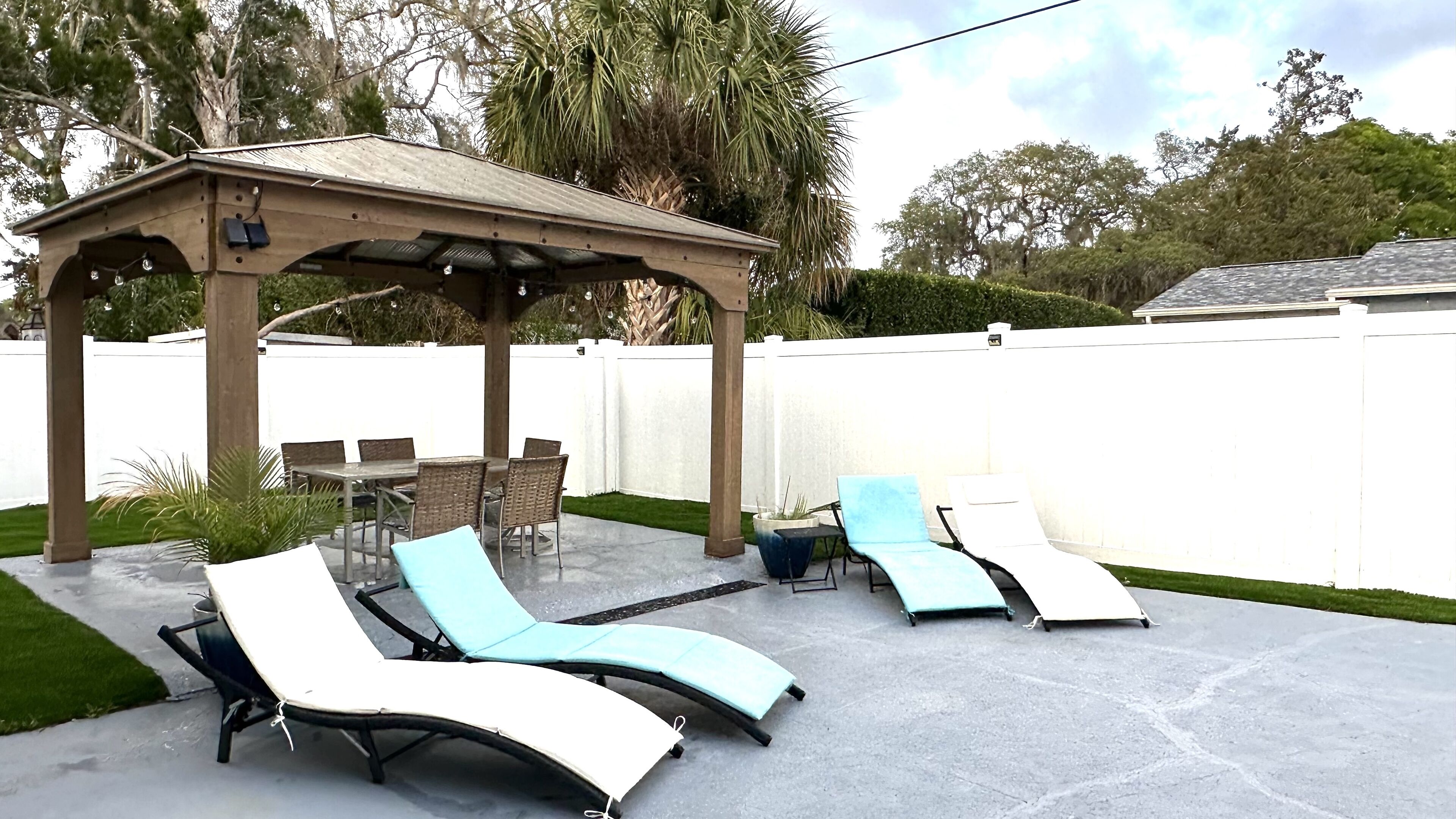 A covered patio area with a pergola, outdoor furniture, and a white fence in the background.