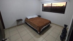 A bedroom with a bed, a nightstand, a window with a view, and a tiled floor. - Excelent apartment, near Downton and Zapopan (Zapopan)