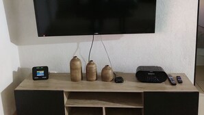 A flat-screen TV mounted on a wall above a wooden entertainment unit with a remote control, a speaker, and decorative vases. - Excelent apartment, near Downton and Zapopan (Zapopan)
