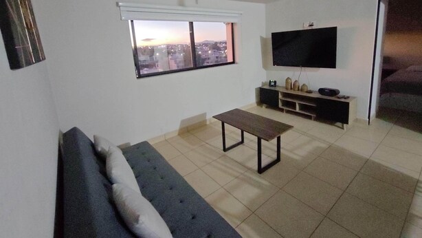 A living room with a sofa, a coffee table, a TV, and a window with a city view. - Excelent apartment, near Downton and Zapopan (Zapopan)
