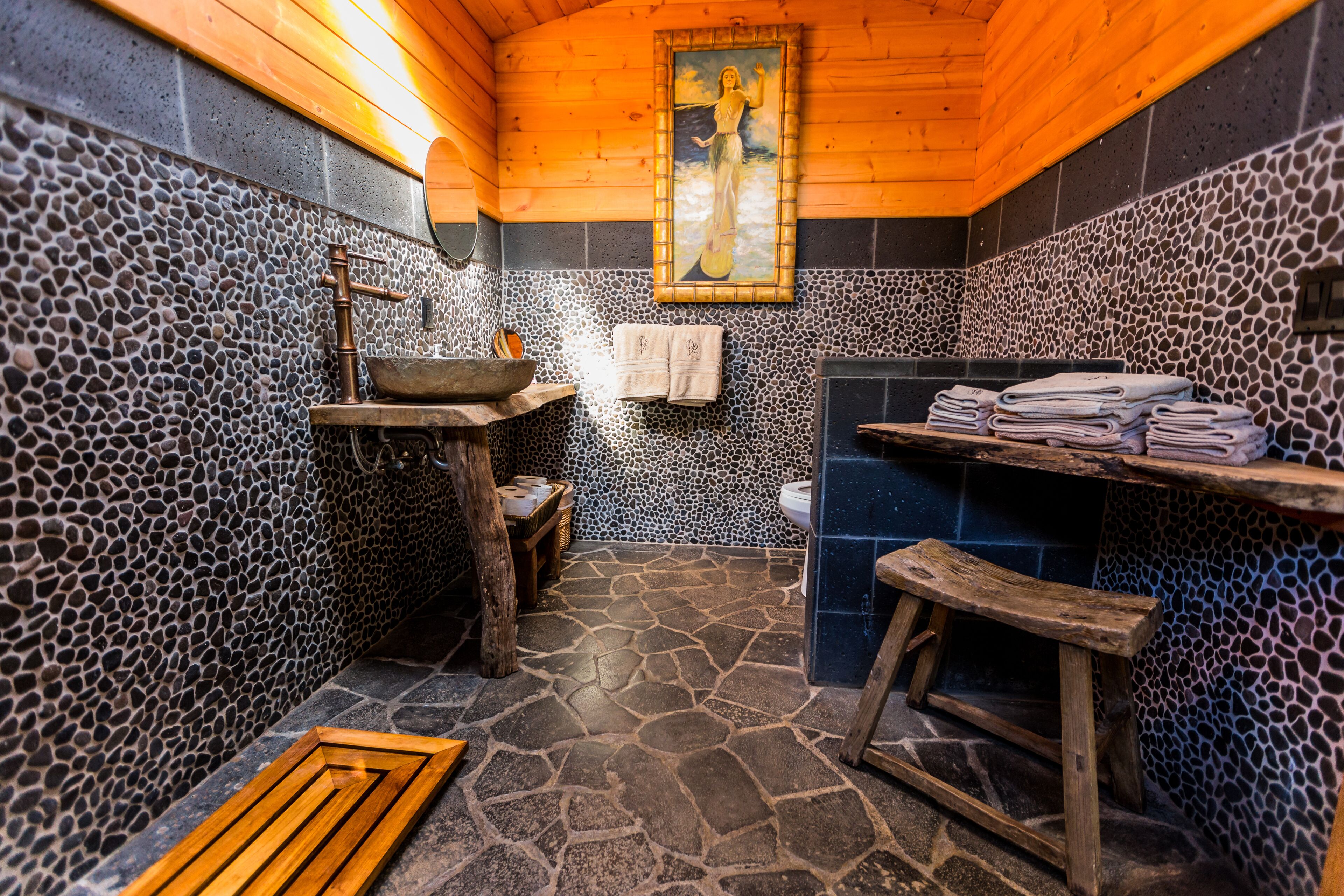 A rustic bathroom with stone walls, a wooden bench, a sink, and a tiled shower area.