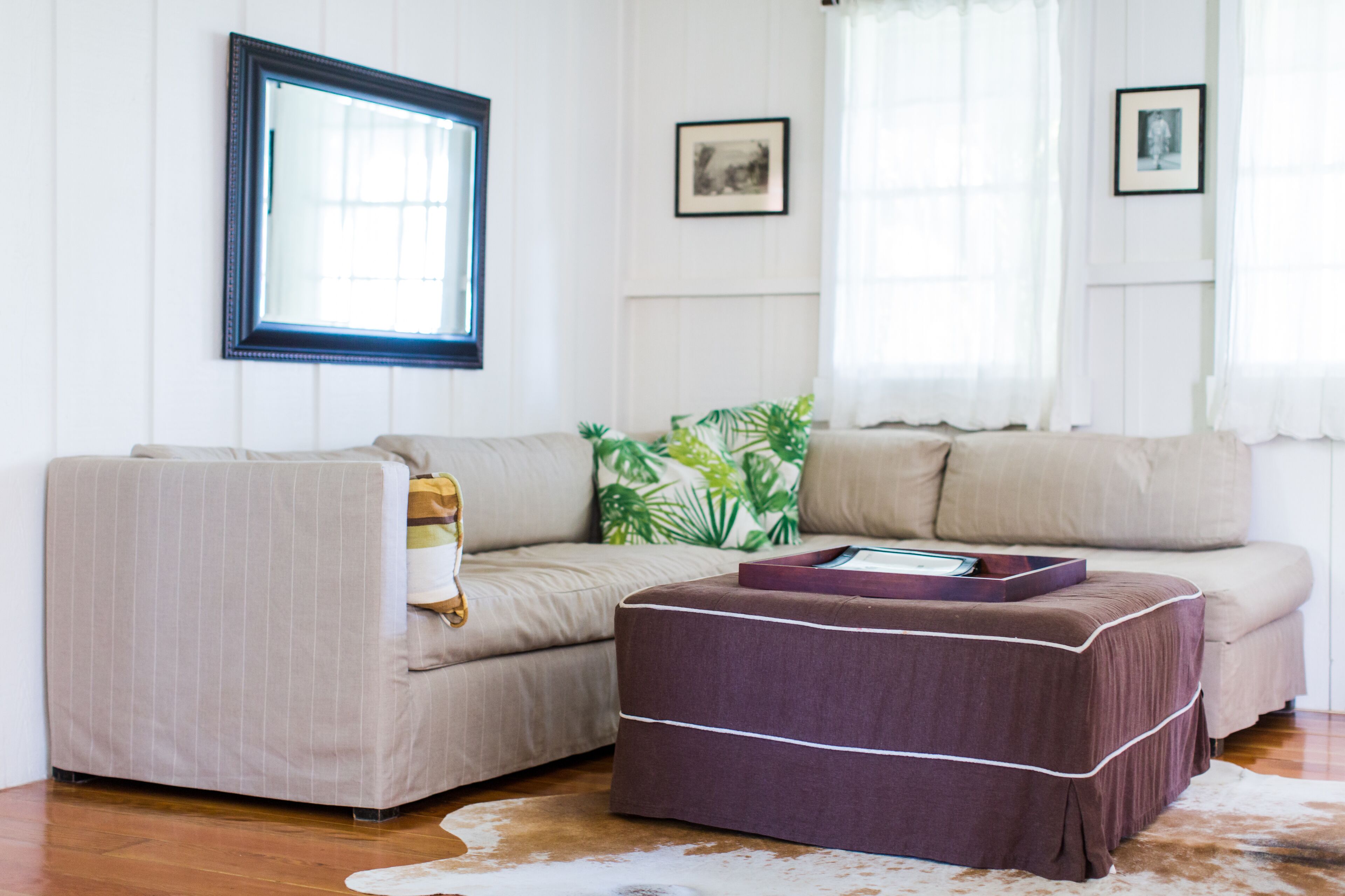 Una sala de estar con sofá, reposapiés y ventana con cortinas.