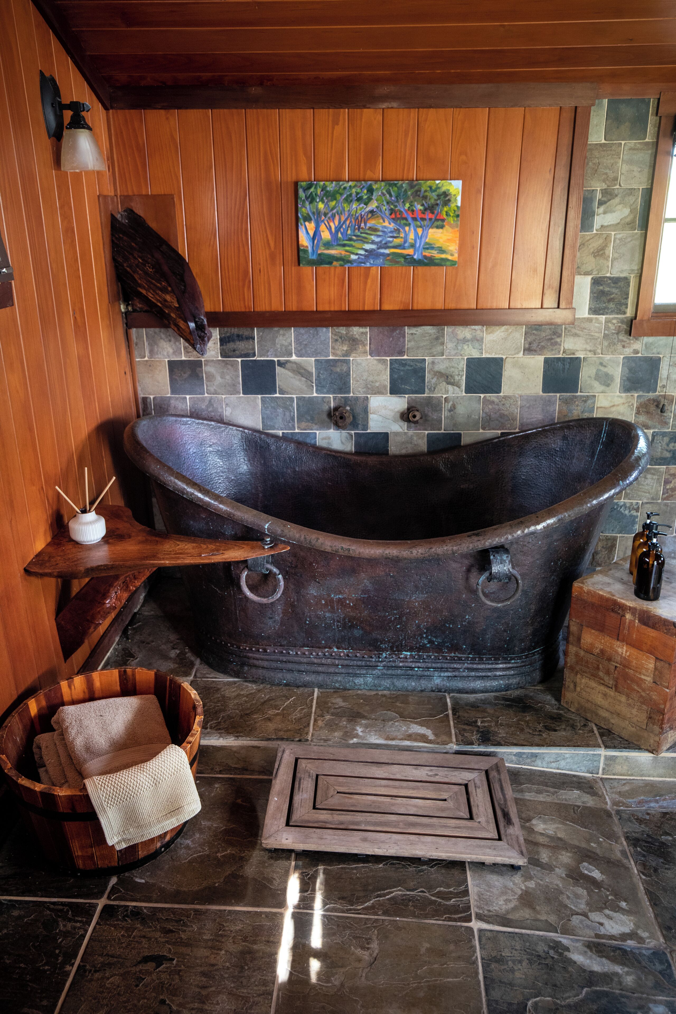 A rustic bathroom with a large, vintage bathtub, wooden accents, and a mosaic tile backsplash.