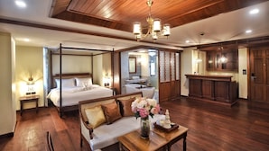 Uma cama com dossel e cortina, uma área de estar com sofá e mesa, um balcão de recepção de madeira e um banheiro com banheira e espelho.