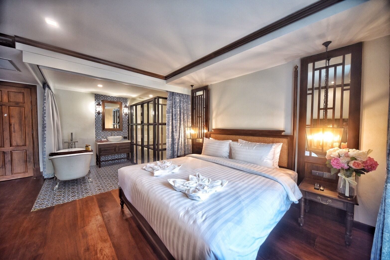 A spacious bedroom with a large bed, a wooden floor, a bathroom with a bathtub, and a mirror.