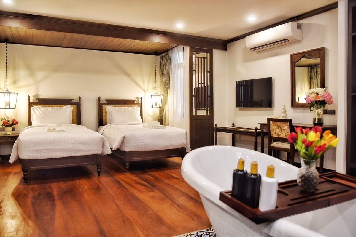 Une chambre d’hôtel avec deux lits, une grande baignoire, un plancher en bois, un bureau avec une chaise et un miroir au mur.