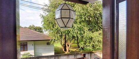 Eine überdachte Veranda mit einer hölzernen Bank und Kissen, einem hängenden Laternen und Blick auf eine Wohngegend mit Bäumen und Häusern.