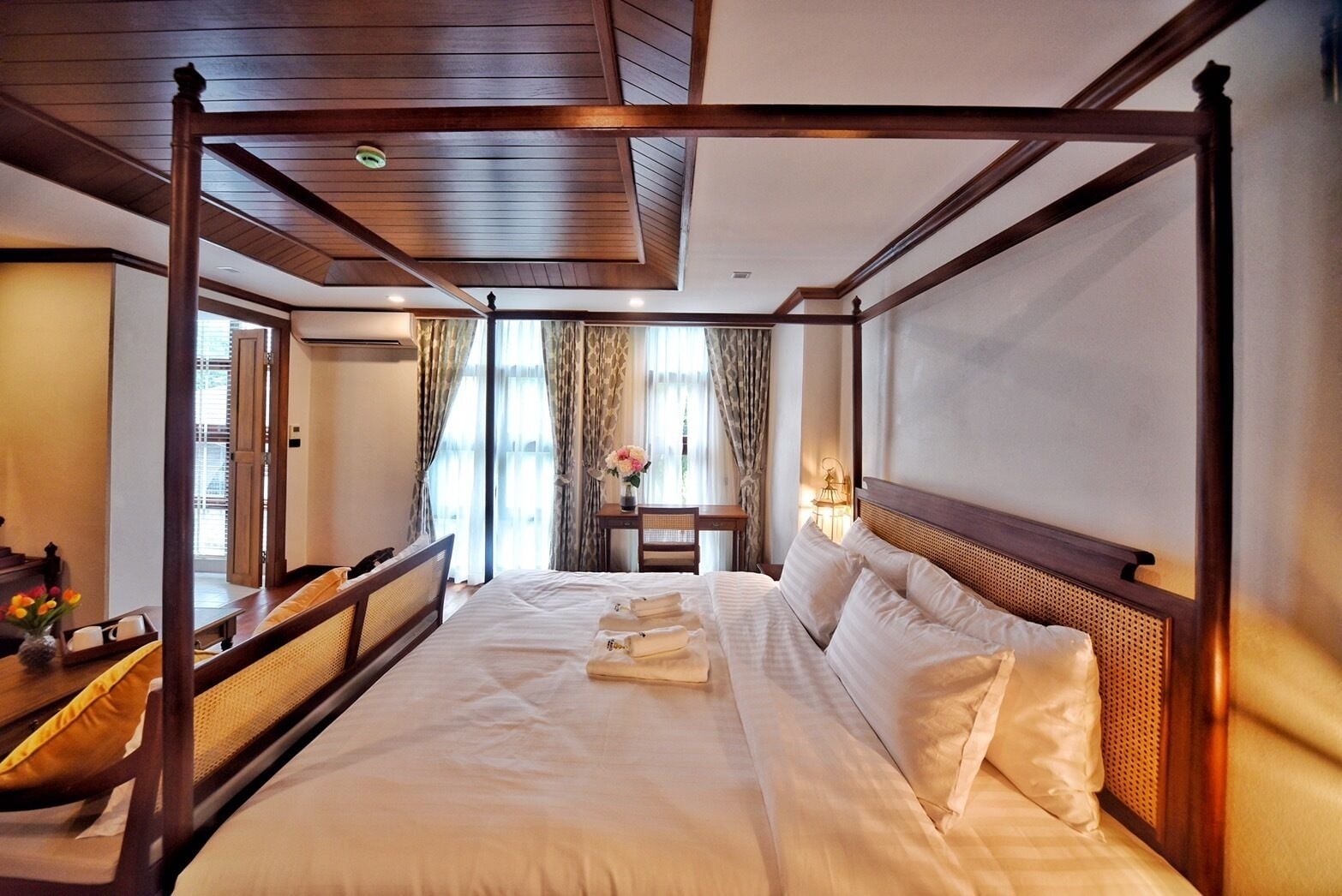 A four-poster bed with a wooden headboard, a bedside table with a lamp, and a window with curtains.