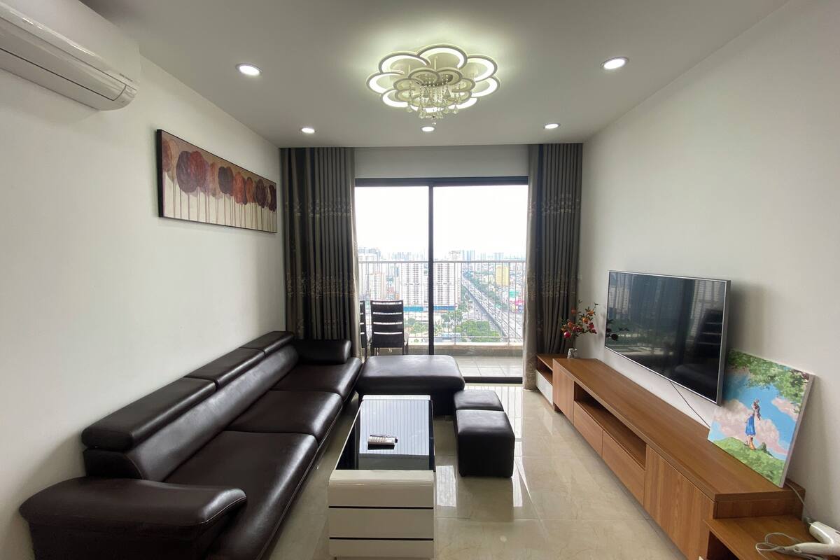 A modern living room with a sofa, a coffee table, a TV, and a balcony with a city view.