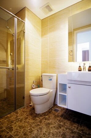 Un baño con cabina de ducha de vidrio, inodoro y lavamanos con espejo.